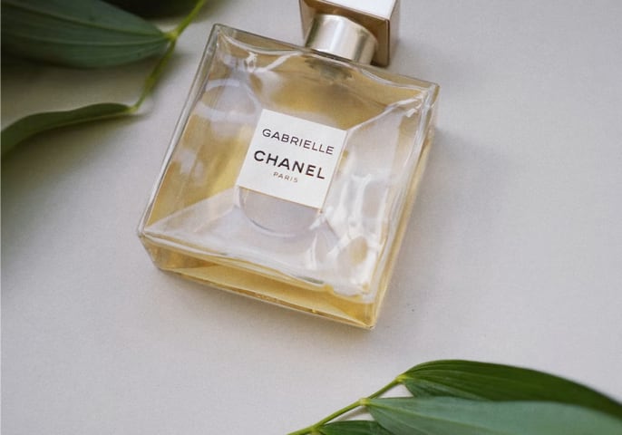 A bottle of CHANEL's Gabrielle Essence Eau De Parfum lays flat on a surface, framed by leaves.